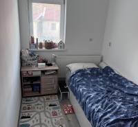 Dětský pokoj s postelí, oknem a koberečkem ve 4-pokojovém bytě.