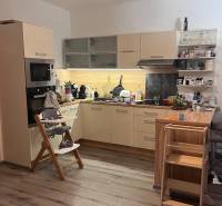 Kuchyně ve 4-pokojovém bytě s podlahou s dřevěným dekorem, dětskou židlí a hračkami.