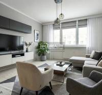 Obývací pokoj ve 3-pokojovém bytě s velkou pohovkou, TV, koberec, podlaha s dřevěným dekorem.