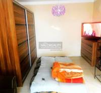 Ložnice v dvoupokojovém bytě s postelí, pohovkou a skříňkou s dřevěným dekorem.