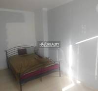 Ložnice s kovovou postelí a bílými stěnami v dvoupokojovém bytě.