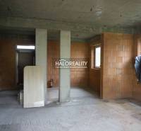 Nedokončený interiér v rodinném domě s odhalenými cihlovými stěnami a betonovými podlahami.