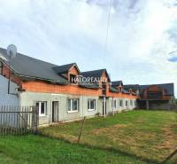 Obchodní prostory v Tibavě, nedokončená budova s travnatým prostorem a plotem.