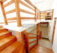 Dřevěné schody a zábradlí v rodinném domě s cihlovým detailem na stěně.