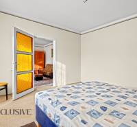 Ložnice v rodinném domě s postelí, křeslem a dveřmi s oranžovým sklem.