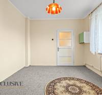 Světlý pokoj v rodinném domě s kobercem a oknem s krajkovou záclonou.