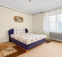 Ložnice v rodinném domě s kobercem, velkým oknem a radiátorem.