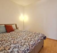 Ložnice v 2-pokojovém bytě s postelí, lampou a podlahou s dřevěným dekorem.