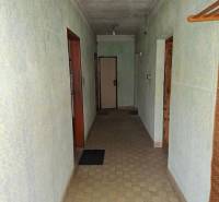 Chodba v rodinném domě se světle zelenými stěnami, dlažbou a jednoduchým osvětlením.