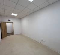 Interiér kanceláře s bílými stěnami, podhledovým stropem a otevřenými dveřmi.