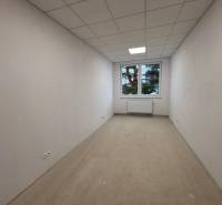 Bílá místnost s oknem, radiátorem a podlahou s dřevěným dekorem v kancelářích.