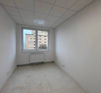 Bílá kancelář s radiátorem a výhledem z okna.