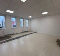 Prázdné kanceláře s bílými stěnami, stropním osvětlením a podlahou s dřevěným dekorem.