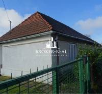 Rodinný dům v Rudabányi s bílou fasádou a šikmou střechou za zeleným plotem.