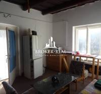 Pokoj v rodinném domě s prosvětleným stolem u okna, křeslem a jídelním stolem.