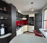 Kuchyně v 1-pokojovém bytě s podlahou s dřevěným dekorem a červeným obkladem.