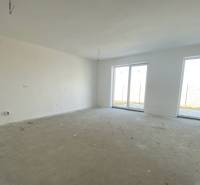 Prostorný pokoj v rodinném domě s betonovou podlahou a velkými okny.