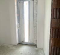 Vstupní dveře v interiéru rodinného domu s betonovou podlahou a neomítnutou cihlovou stěnou.