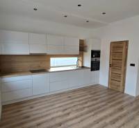 Kuchyně s bílými skříňkami a dřevěným dekorem v rodinném domě, podlaha s dřevěným dekorem.