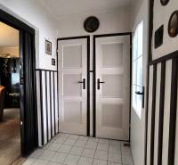 Interiér rodinného domu s bílými dveřmi, dlažbou a tmavým obkladem stěn.