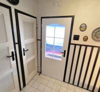 Interiér rodinného domu s bílými dveřmi, dekoracemi na stěně a dlažbou.