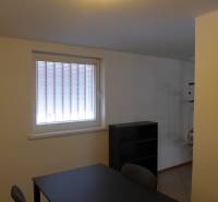 Kancelářský prostor se stolem a regálem, sklady a haly, světlá atmosféra.