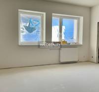 Pokoj v rodinném domě s okny a radiátorem, nevyužitý prostor připravený k dokončení.