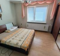 Ložnice v rodinném domě s postelí, skříní a podlahou s dřevěným dekorem.