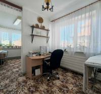 Pokoj v rodinném domě s psacím stolem, rostlinami a kobercem s květinovým vzorem.