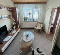 Obývací pokoj v rodinném domě s kobercem, televizí a skleněným stolkem.