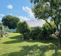 Zahrada rodinného domu v Partizánském s udržovaným trávníkem, stromy a zákoutím na posezení.