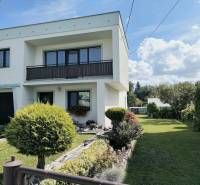 Rodinný dům v Partizánském obklopený zahradou s dřevinami a zeleným trávníkem.