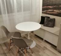 Jídelní kout s kulatým stolem, dvěma židlemi a dekoračními polštáři, podlaha s dřevěným dekorem.