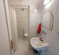 Koupelna v kancelářích se zrcadlem, umyvadlem a toaletou na bílých obkladech.