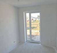 Bílá místnost v rodinném domě s velkým oknem a výhledem na zahradu.