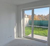 Interiér rodinného domu s velkým oknem do zahrady, bílé stěny a podlaha.