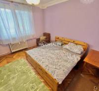 Ložnice ve 4pokojovém bytě s postelí, křeslem a podlahou s dřevěným dekorem.