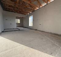 Interiér rodinného domu s betonovou podlahou, dřevěnými trámy a rozvody elektřiny.