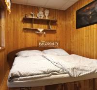 Ložnice na chatě s dřevěnou stěnou a policemi nad postelí.