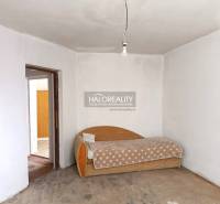 Interiér rodinného domu se starší pohovkou a surovou betonovou podlahou.