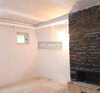 Interiér rodinného domu s kamenným krbem a malým oknem.