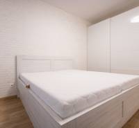 Světlá ložnice s bílou postelí, vestavěná skříň, podlaha s dřevěným dekorem v 2-pokojovém bytě.