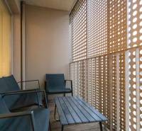Balkon s dřevěným dekorem, posezením a perforovanou stěnou v 2-pokojovém bytě.