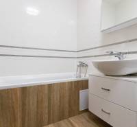 Koupelna v 2-pokojovém bytě s vanou, umyvadlem a podlahou s dřevěným dekorem.