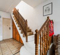 Interiér rodinného domu se schodištěm, sytě červeným kobercem a obrazem na stěně.