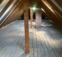 Podkroví v chatě s dřevěnými trámy a cihlovým komínem, podlaha s dřevěným dekorem.