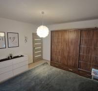 Ložnice ve 3-pokojovém bytě s podlahou s dřevěným dekorem, bílý nábytek, dekorace na stěnách.