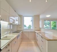 Kuchyně v 3-pokojovém bytě s velkým oknem, bílými skříňkami a lesklou pracovní deskou.