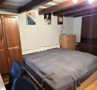 Ložnice v rodinném domě s dřevěným trámovým stropem, nábytkem a dekorativními obrazy.