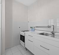 Kuchyně v 1-pokojovém bytě s bílou kuchyňskou linkou a sporákem.